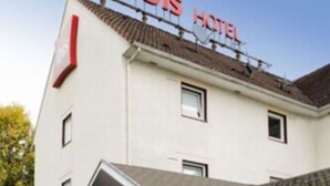 Un hotel con fachada blanca, un área de estar al aire libre techada con mesas y sillas, y un letrero que dice "ibis HOTEL".