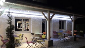 Un patio al aire libre con mesas y sillas, una planta en maceta y una ventana que da al interior.