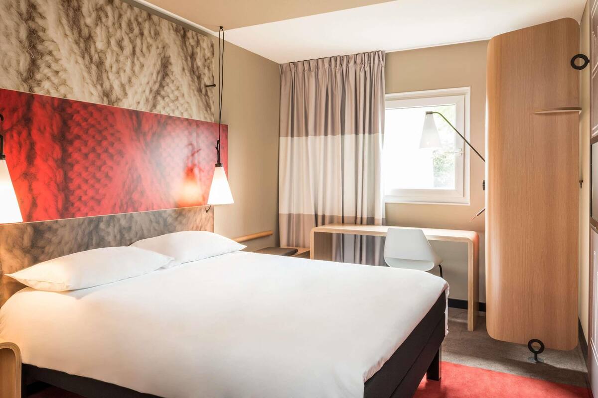 Een hotelkamer met een bed, bureau en kledingkast.