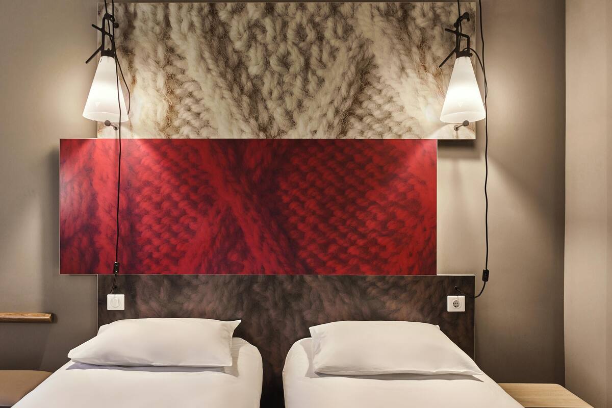Een hotelkamer met twee bedden, een grote tv aan de muur en twee bedlampen.