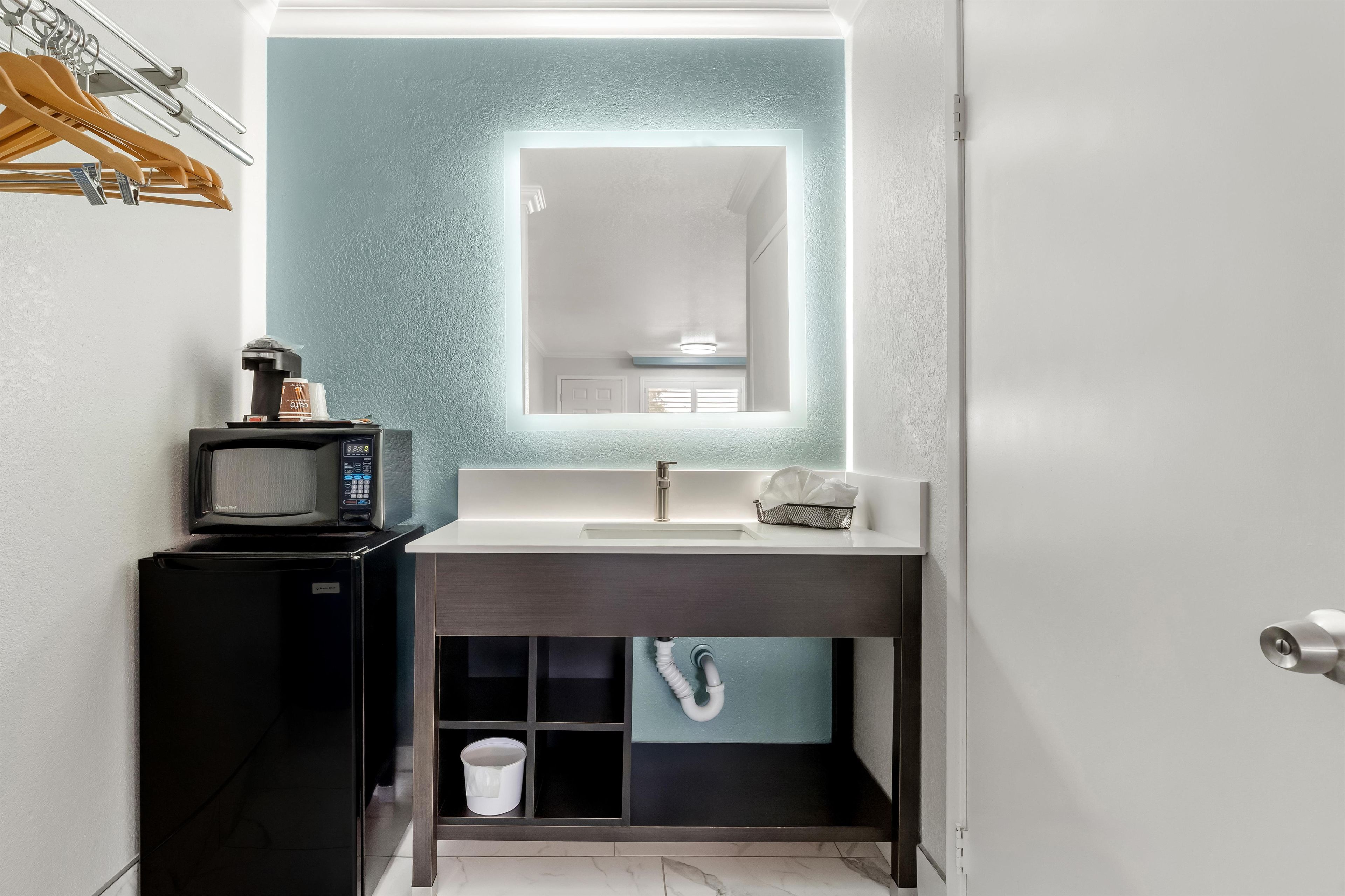 A compact bathroom with a built-in sink, a mirror, a coffee machine, and a towel rack.