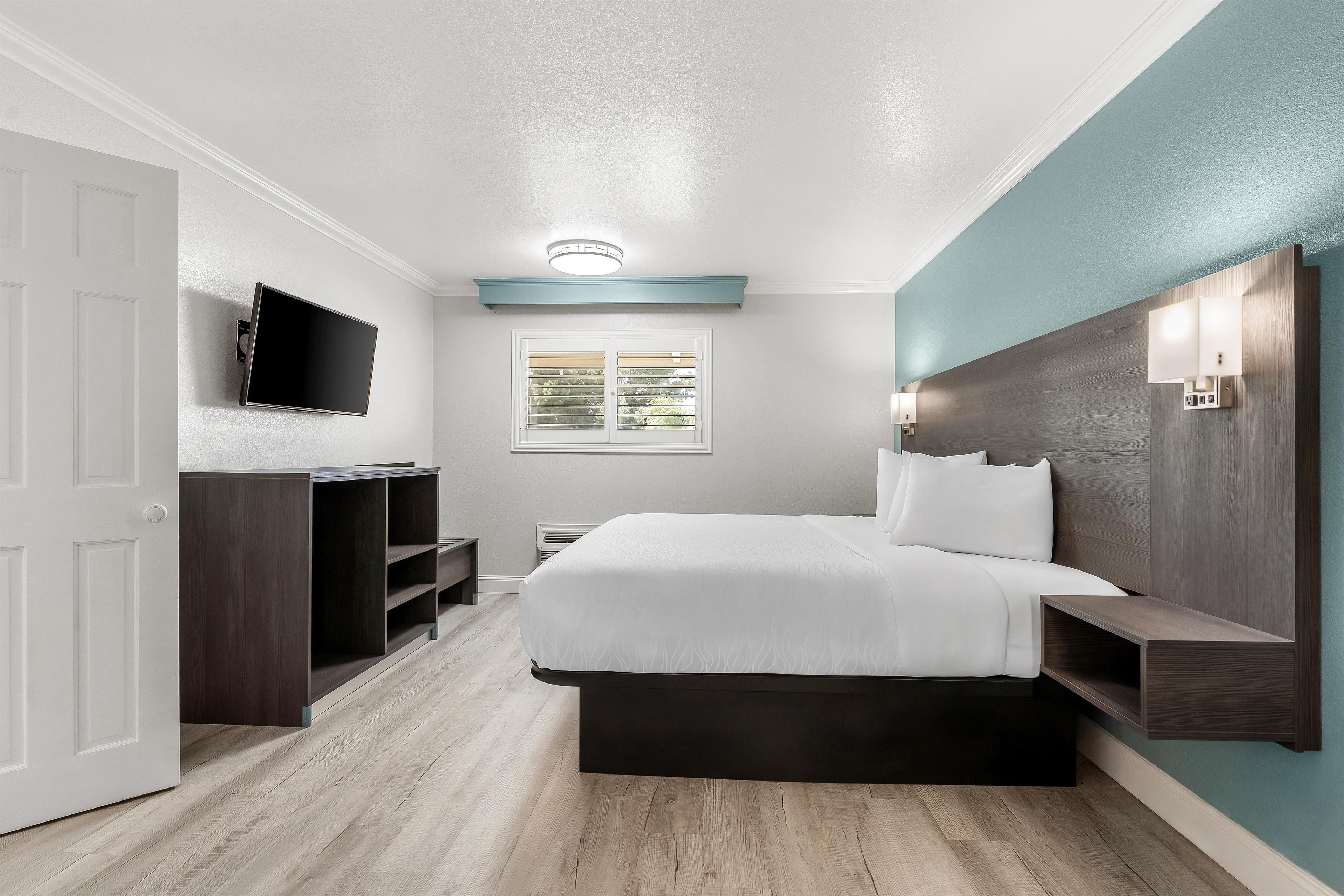 Un dormitorio moderno con cama, televisor, ventana y estanterías empotradas.