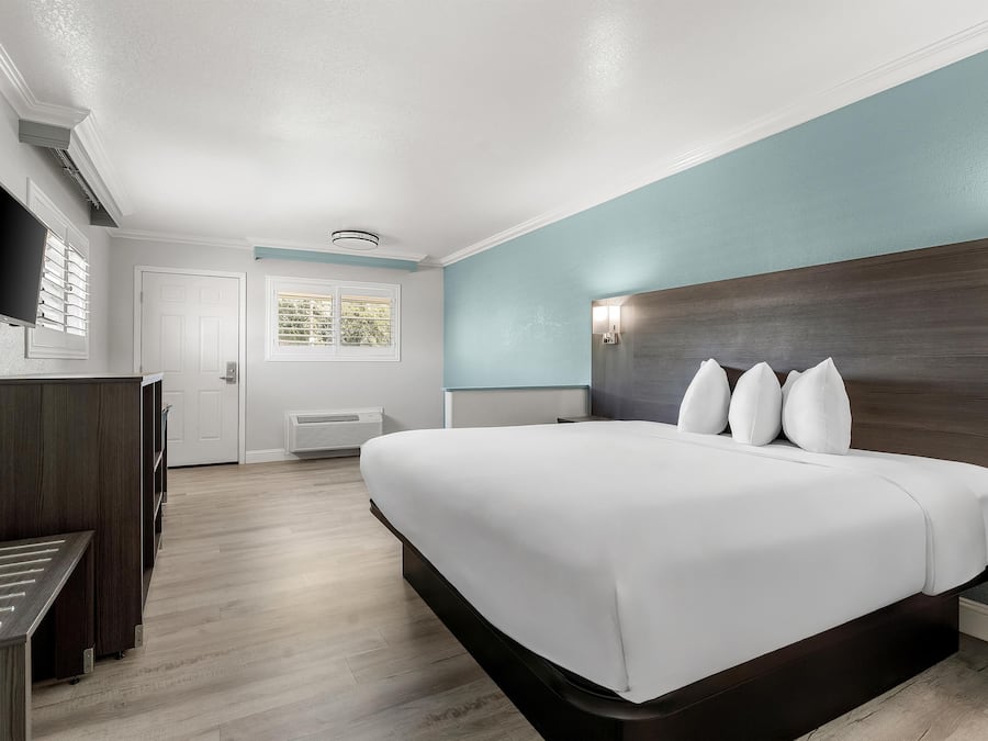 A hotel room with a large bed, a desk, a television, and a window with blinds.