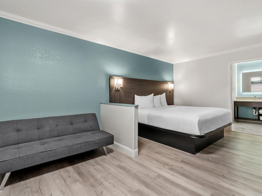 A hotel room with a bed, a sofa, a nightstand, and a bathroom mirror.