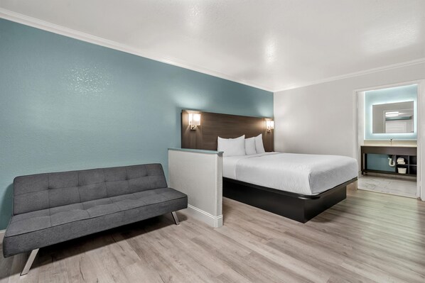 A hotel room with a bed, a sofa, a nightstand, and a bathroom mirror.