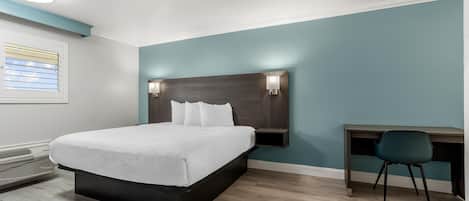 A hotel room with a bed, bedside table, chair, and a desk with a chair.