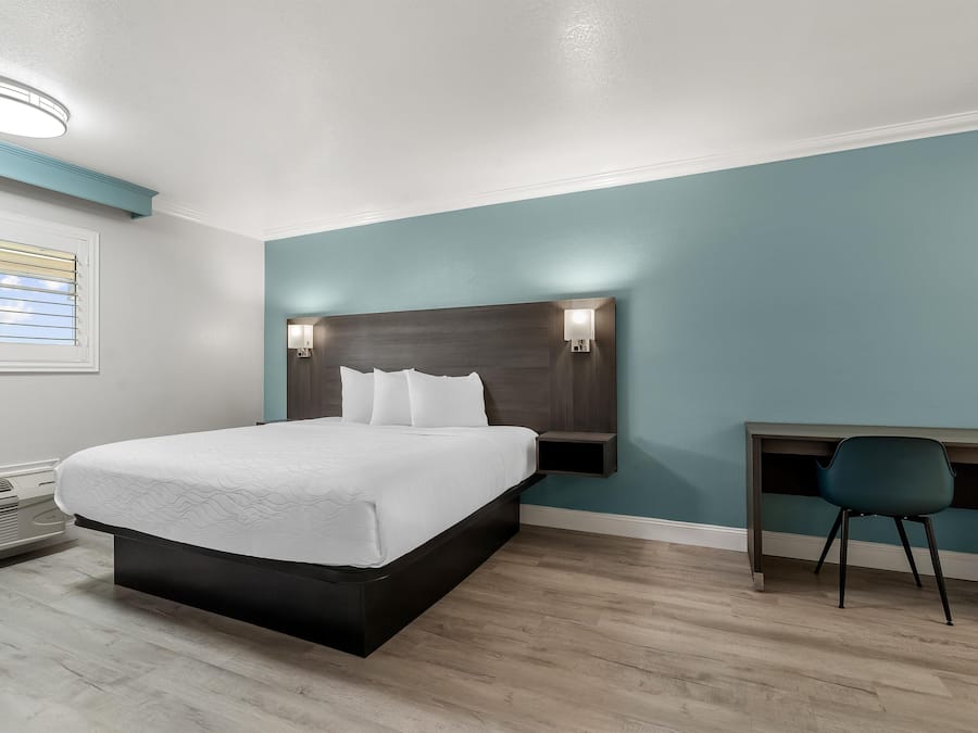 Una habitación de hotel con cama, mesita de noche, silla y escritorio con otra silla.