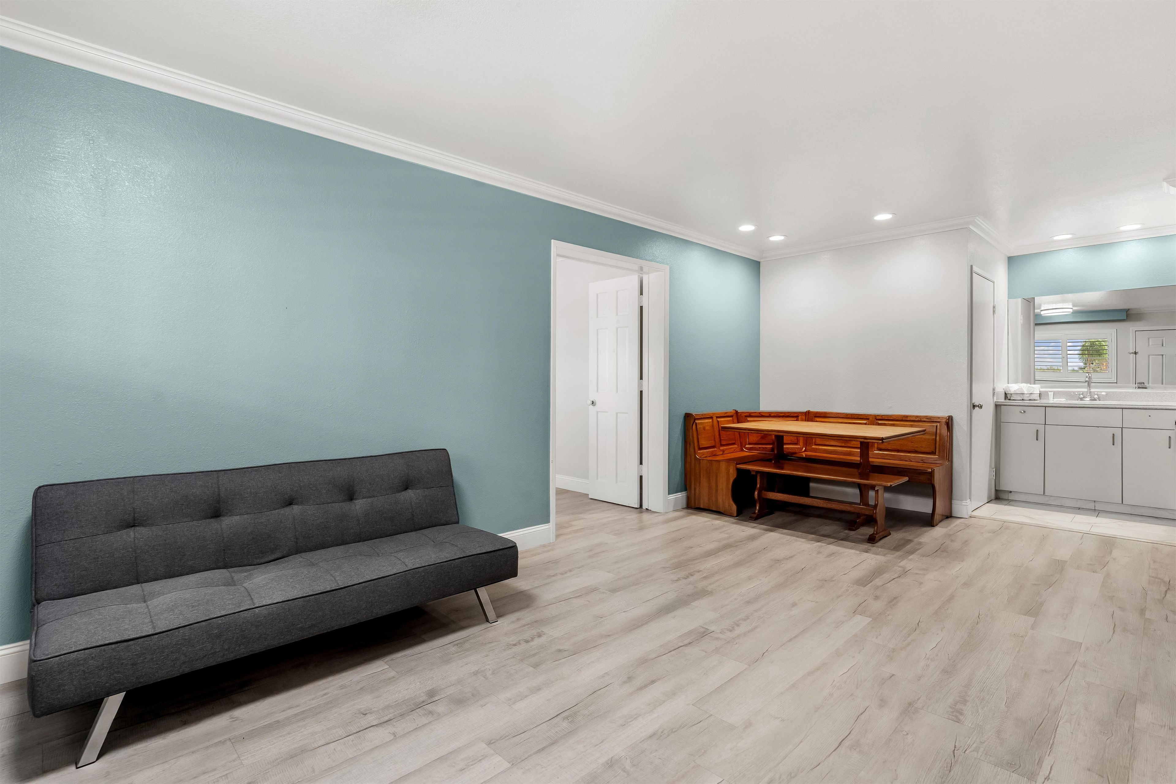 Una sala de estar moderna con un sofá gris, una mesa de comedor de madera y una zona de cocina con armarios y una ventana.
