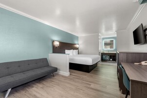 Quarto de hotel moderno com cama, sofá, escrivaninha e televisão.