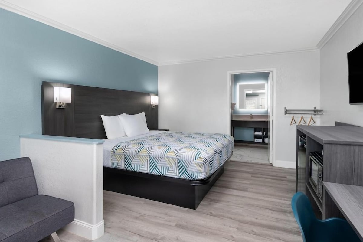 Ein modernes Hotelzimmer mit Bett, Schreibtisch, Stuhl und Fernseher.
