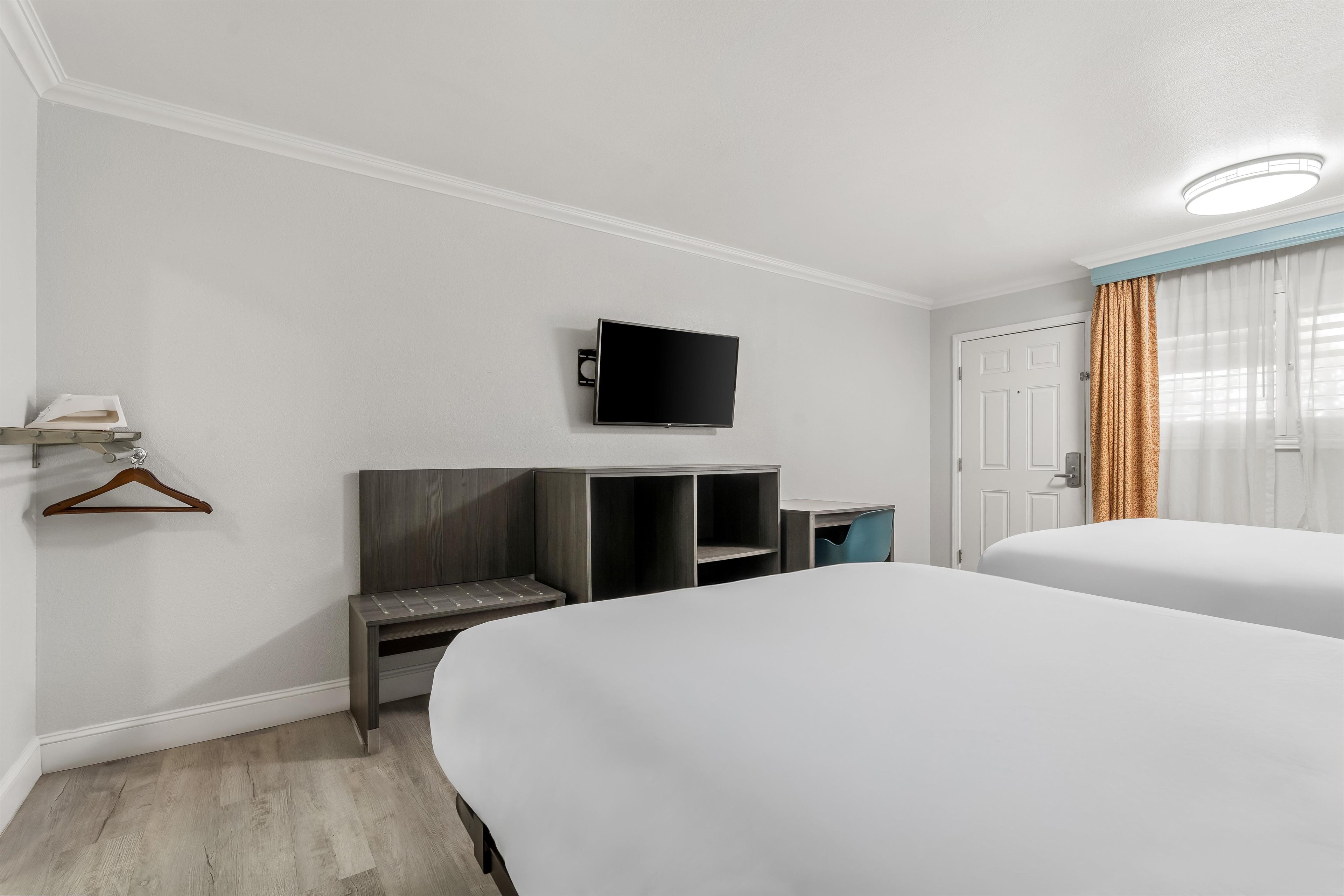 A hotel room with two beds, a TV mounted on the wall, a desk with a chair, and a wardrobe.