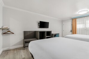 Een hotelkamer met twee bedden, een aan de muur bevestigde televisie, een bureau met stoel en een kledingkast.