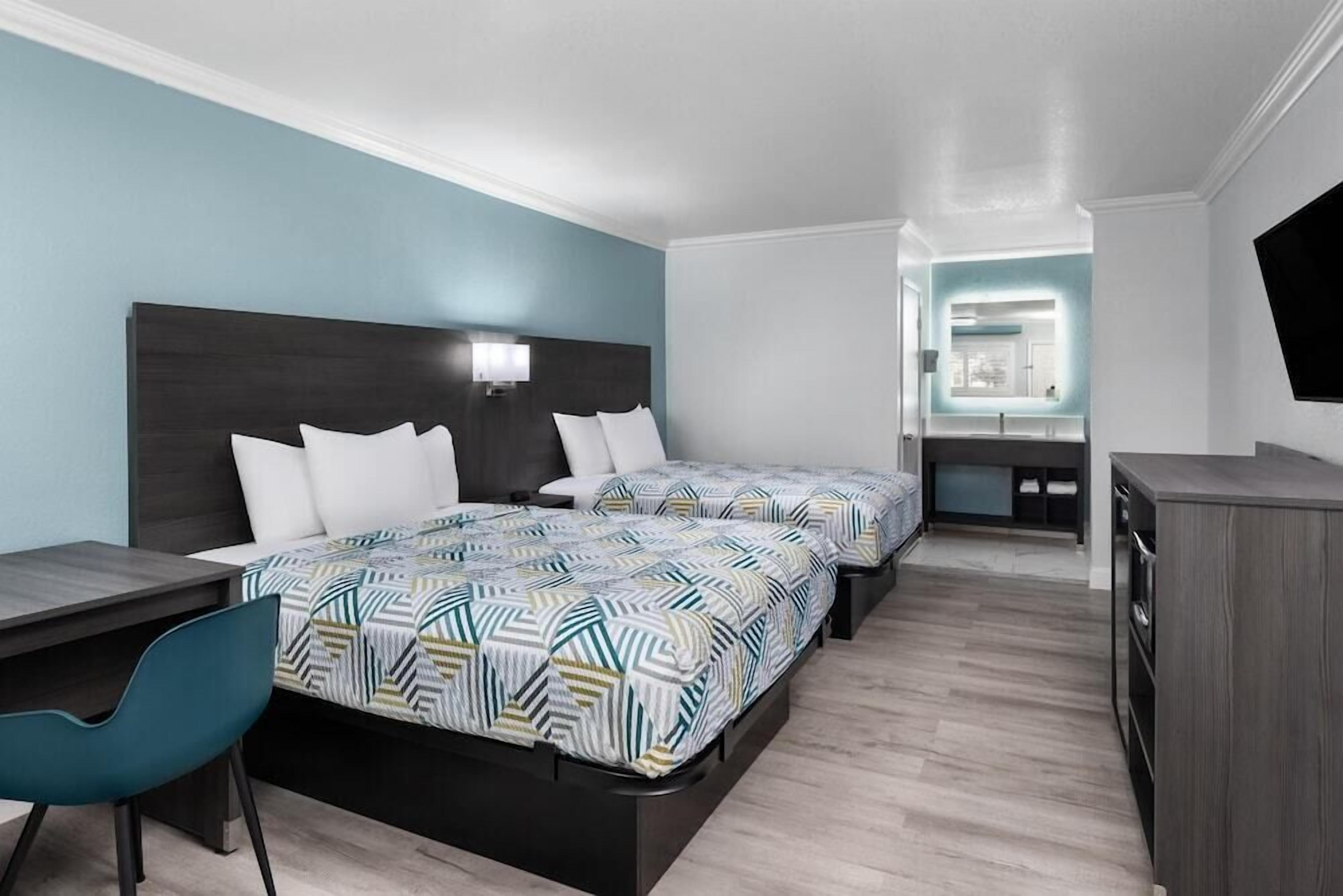 Una habitación de hotel moderna con dos camas, un escritorio, una silla y un televisor.