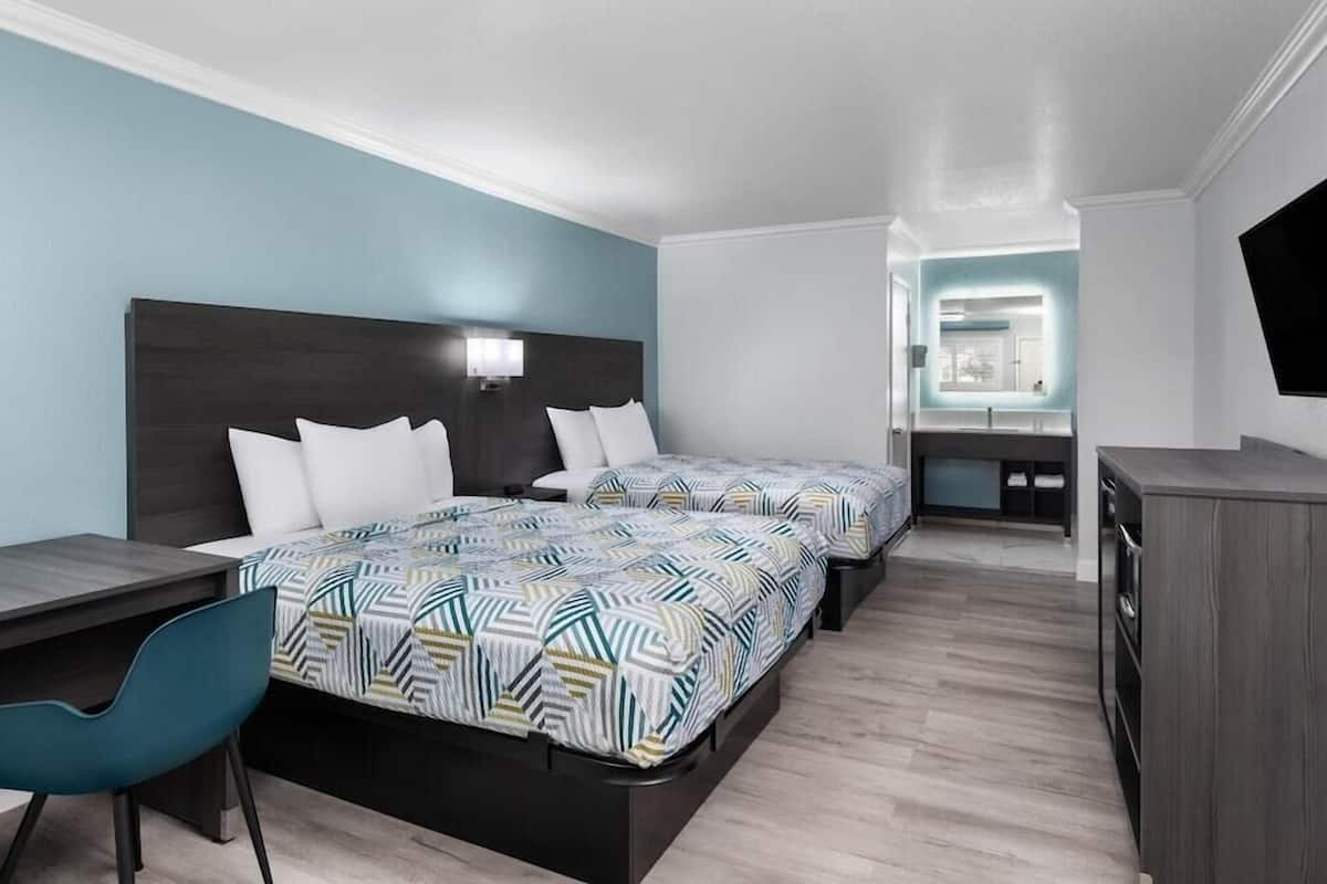 Ein modernes Hotelzimmer mit zwei Betten, einem Schreibtisch, einem Stuhl und einem Fernseher.