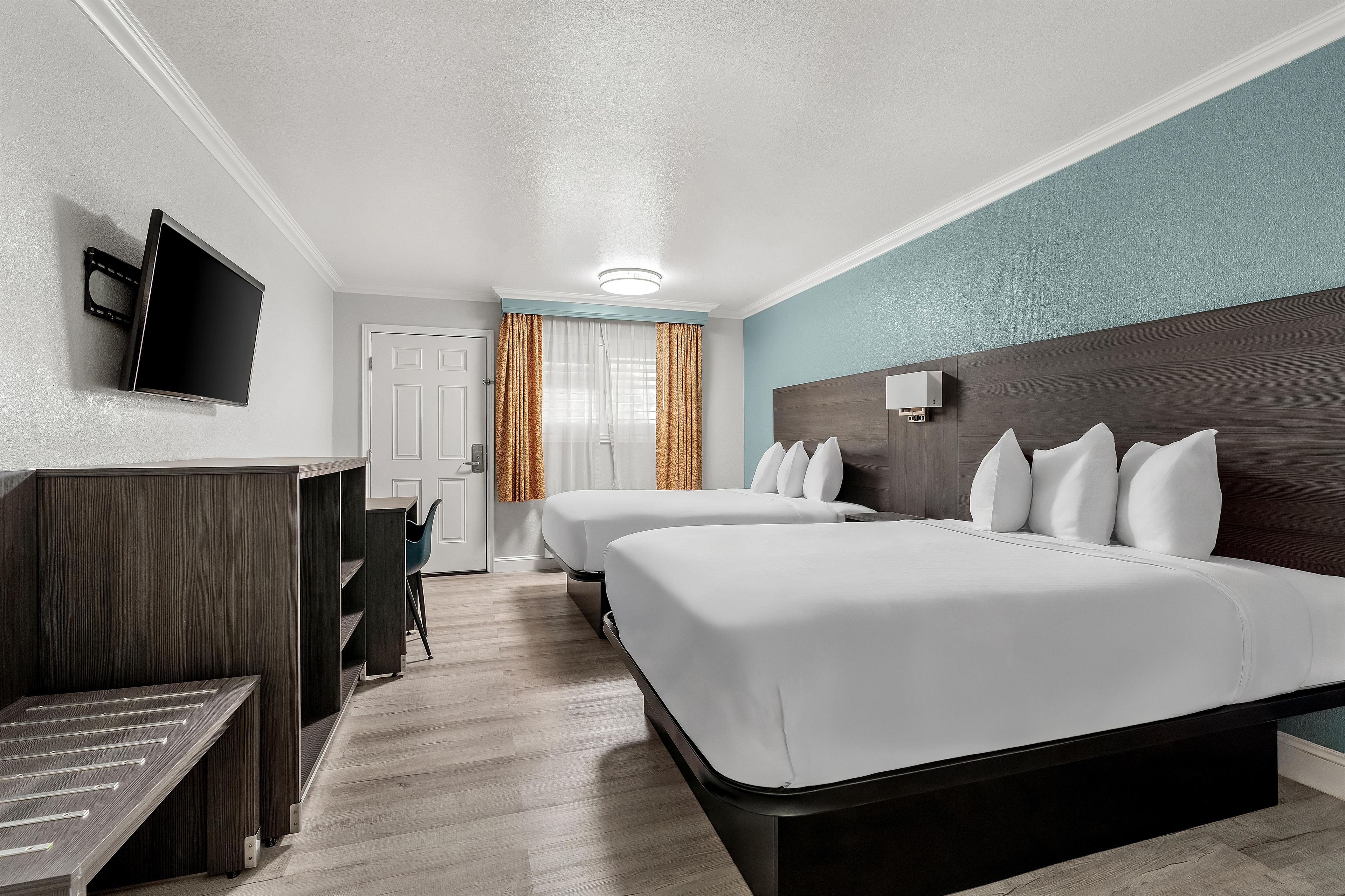 A hotel room with two beds, a desk, a TV, and a bathroom visible through the door.