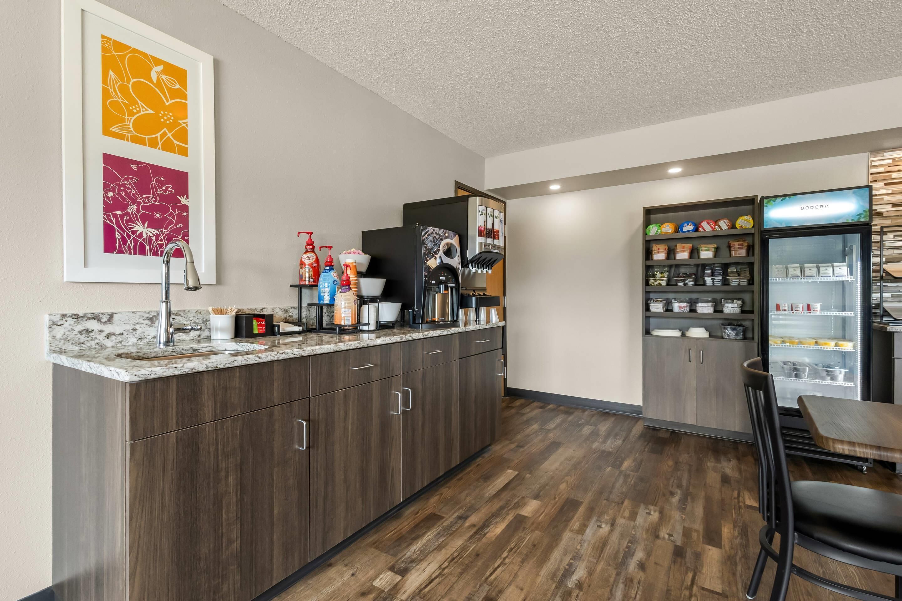 A modern kitchen with a marble countertop, dark wood cabinets, a coffee machine, and a refrigerator stocked with beverages.
