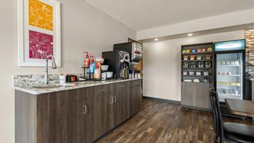 A modern kitchen with a marble countertop, dark wood cabinets, a coffee machine, and a refrigerator stocked with beverages.