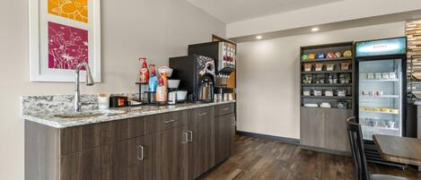A modern kitchen with a marble countertop, dark wood cabinets, a coffee machine, and a refrigerator stocked with beverages.