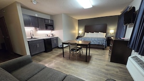 Une chambre d’hôtel compacte comprenant un coin cuisine, un lit avec une tête de lit, une table à manger avec des chaises et un canapé.