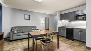 Una cocina compacta con armarios oscuros, un microondas y una zona de comedor con mesa y sillas.