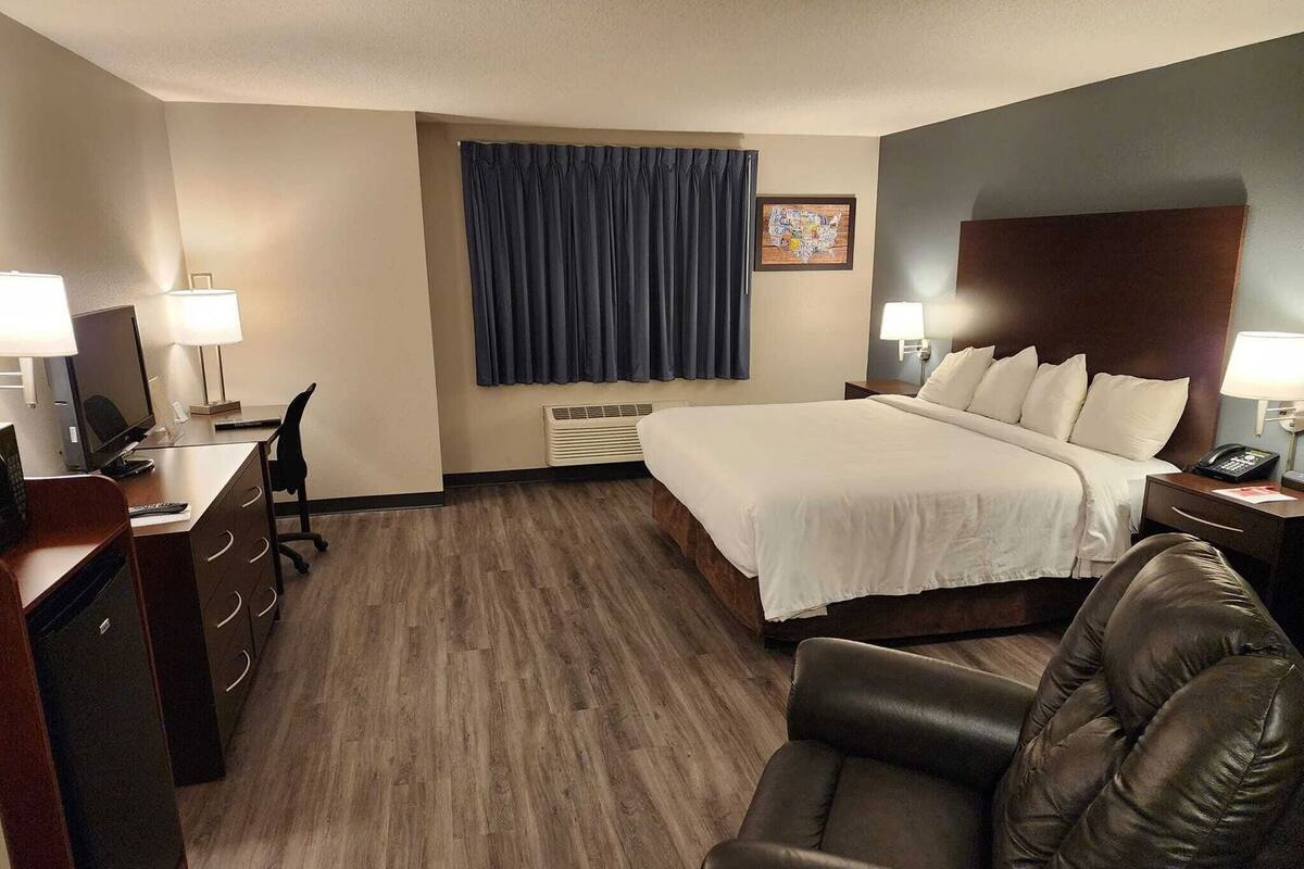 A hotel room with a bed, desk, chair, and a large window with curtains.
