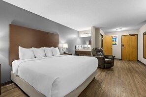 Habitación de hotel con una cama grande, un escritorio con lámpara, un sillón de cuero y un baño con espejo y toallero.