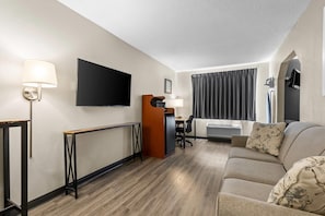 A hotel room with a sofa, a TV, a desk with a chair, a lamp, and a window with curtains. - Park Inn by Radisson (Ortonville)