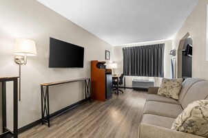 Habitación de hotel con sofá, televisión, escritorio con silla, lámpara y ventana con cortinas.