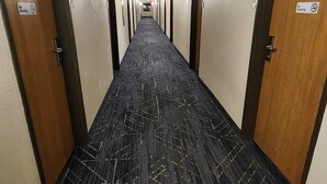 Un couloir d’hôtel avec des revêtements de sol en moquette, des portes des deux côtés et des panneaux indiquant qu’il est interdit de fumer.