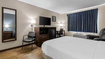 Habitación de hotel con una cama grande, un escritorio con silla, un televisor, un espejo y una ventana con cortinas.