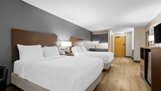 Une chambre d’hôtel avec deux lits, un bureau, une chaise, une télévision et une kitchenette.