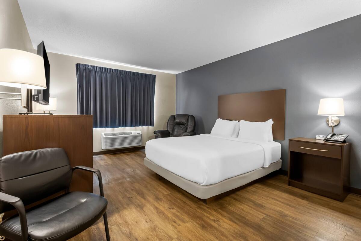 A hotel room with a bed, a desk, a chair, a TV, a lamp, and a window with curtains.