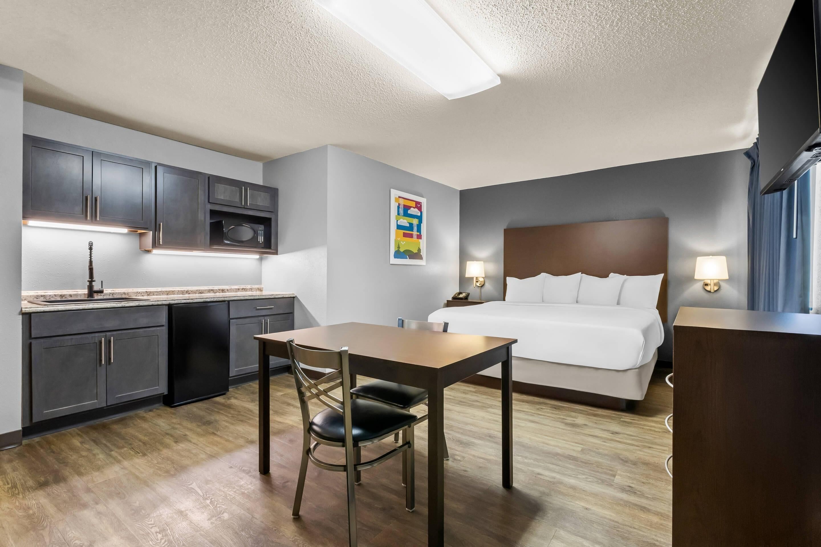 A hotel room with a bed, bedside lamps, a desk with a chair, a microwave, and cabinets.