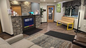 Un espace d’accueil avec un mur en pierre, un écran numérique, un banc et un tapis à motifs.