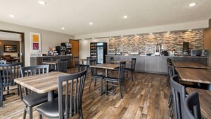 Un restaurant moderne avec des tables et des chaises en bois, un espace cuisine et un mur de fond en pierre.