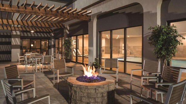 An outdoor patio area with a stone fire pit, wooden chairs, and tables. - Country Inn & Suites by Radisson, La Crosse, WI (La Crosse)