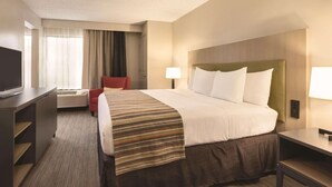 A hotel room with a large bed, a desk with a flat-screen TV, a chair, a lamp, and a window with curtains. - Country Inn & Suites by Radisson, La Crosse, WI (La Crosse)