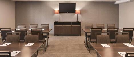A conference room with a long table, chairs, a TV, and a podium.