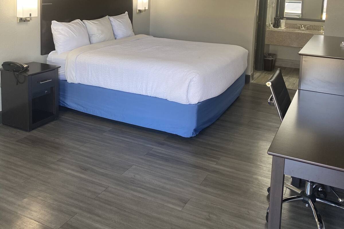 A hotel room with a large bed, bedside tables, a desk, and a mirror.