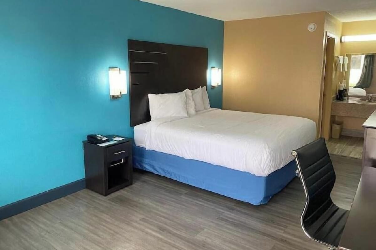 Une chambre d’hôtel avec un lit, une table de chevet, une chaise et une salle de bain visible à travers une porte ouverte.