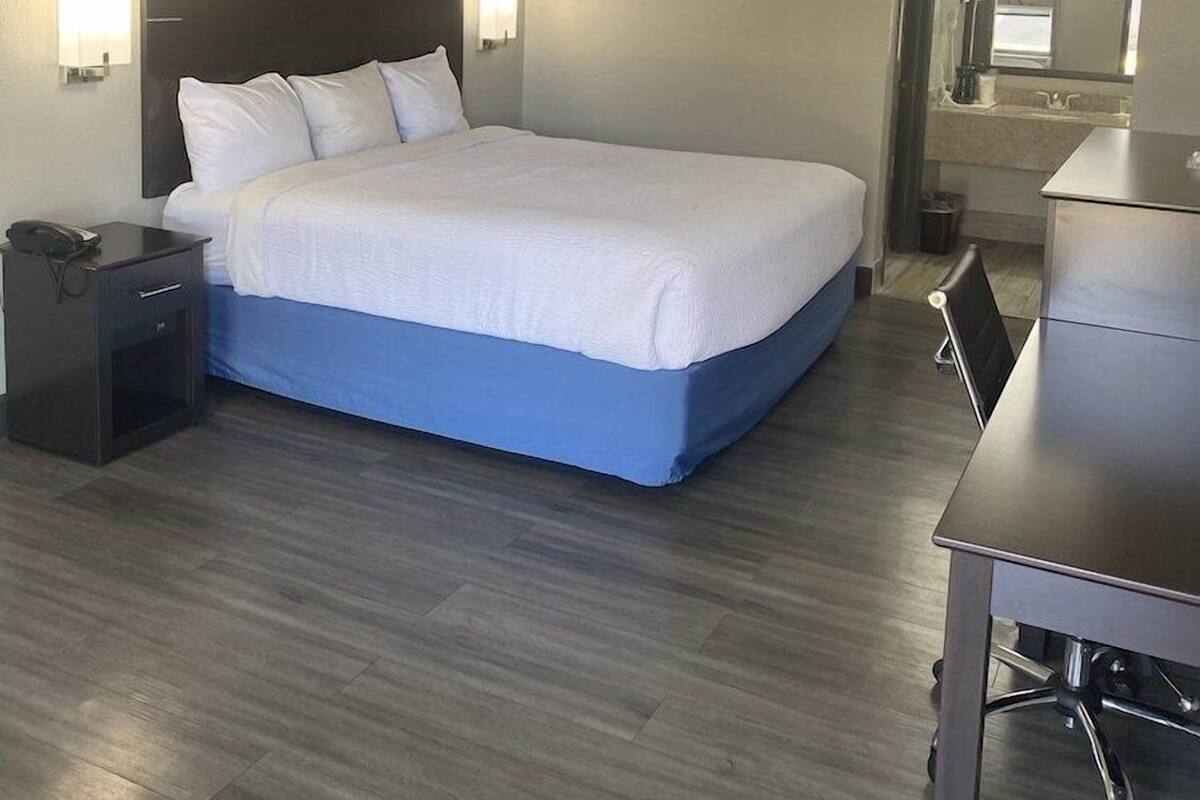 A hotel room with a bed, bedside table, lamp, desk, chair, and a mirror.