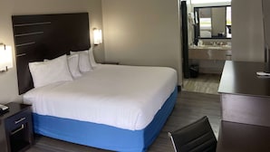 Une chambre d’hôtel avec un grand lit, une table de chevet, un bureau et une salle de bain visible à travers une porte ouverte.
