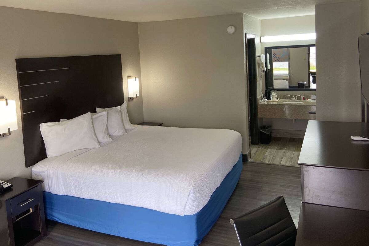 A hotel room with a large bed, a nightstand, a desk, and a bathroom visible through an open door.