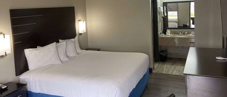 Una habitación de hotel con una cama grande, una mesita de noche, un escritorio y un baño visible a través de una puerta abierta.