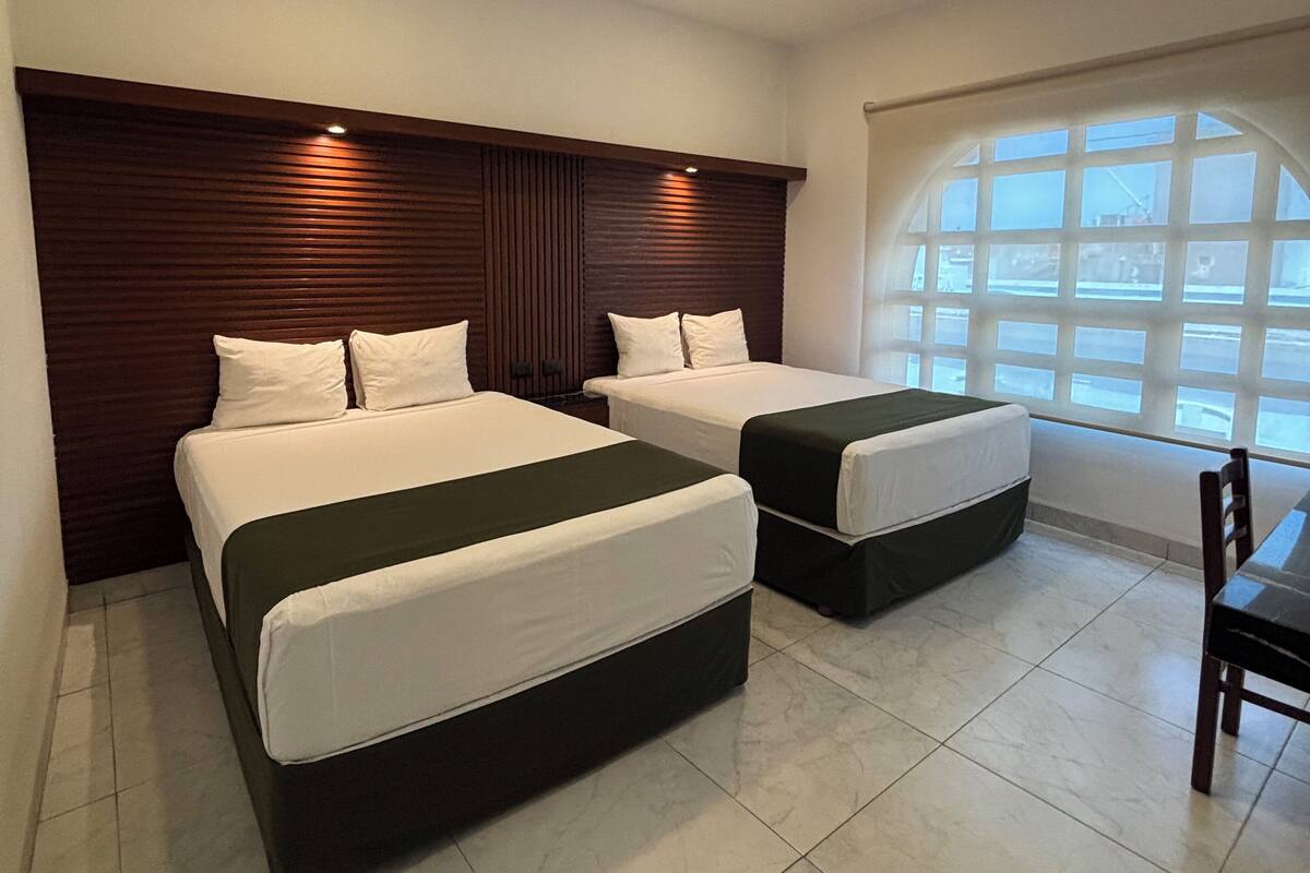 A hotel room with two beds, a wooden headboard, a window with a view, and a tiled floor.