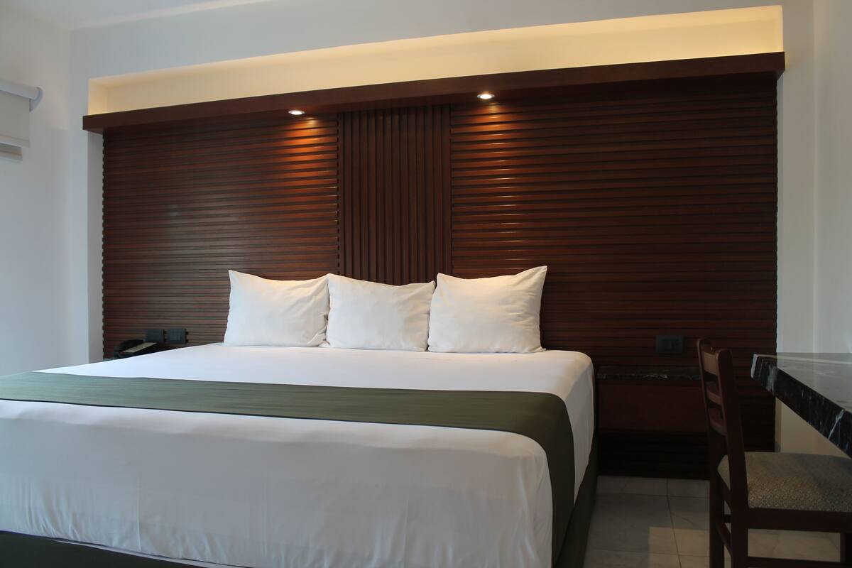 A hotel room with a large bed, a wooden headboard, and a small desk with a chair.