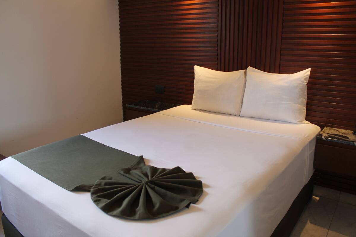 A neatly made bed with white linens and a green throw blanket.