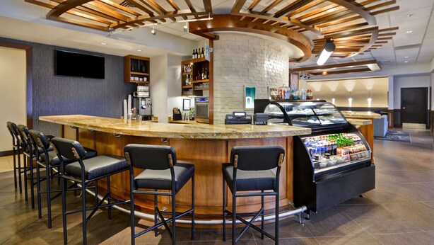 A bar area with a curved counter, bar stools, a beverage dispenser, and a television mounted on the wall. - Hyatt Place Columbus/Worthington (Columbus)