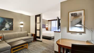 A hotel room with a sofa, a desk, a bed, and a painting on the wall.