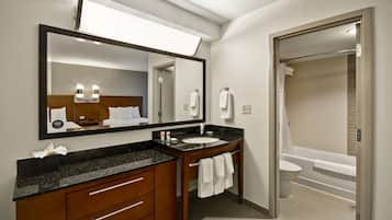 A modern bathroom with a large mirror, two sinks, a toilet, and a bathtub.